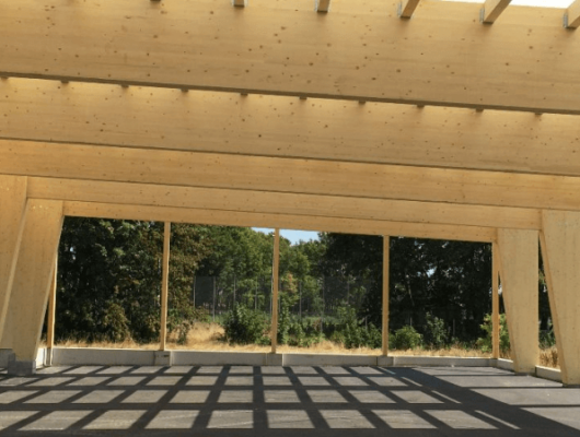 Holzstruktur mit Dach und Gehweg, die als Carport dient und Schutz für Fahrzeuge bietet.