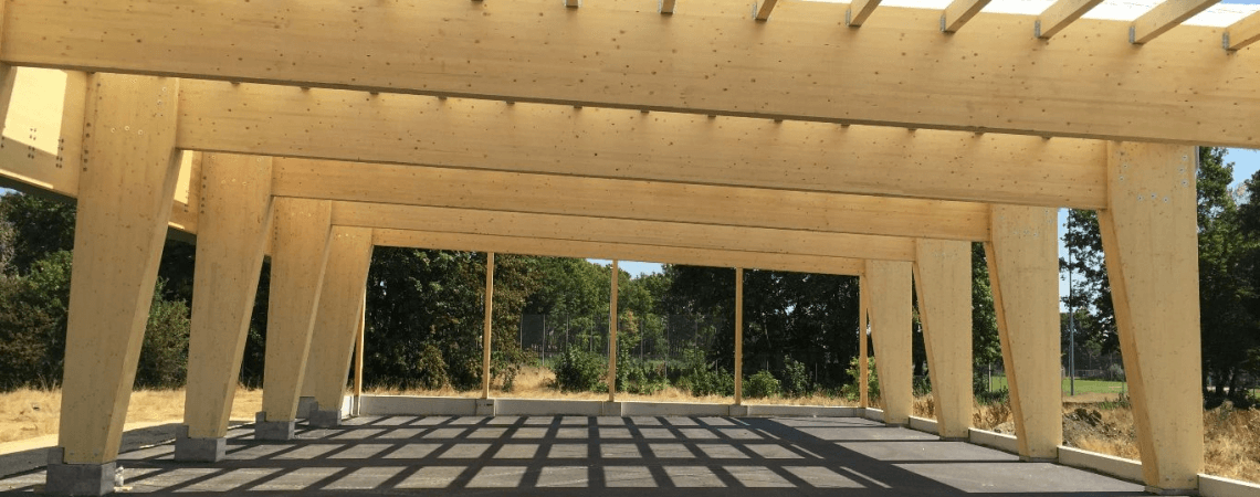 Holzstruktur mit Dach und Gehweg, die als Carport dient und Schutz für Fahrzeuge bietet.