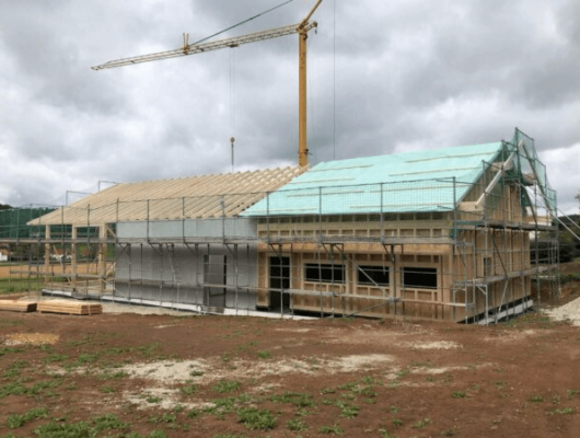 Ein Kran hebt Materialien für ein Haus, das sich im Bau befindet, und zeigt die Fortschritte der Konstruktion.