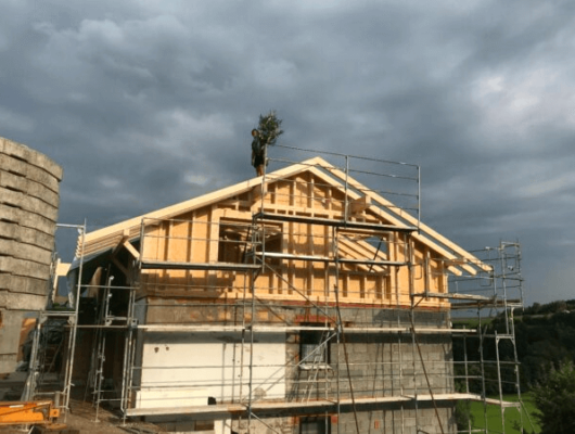 Ein im Bau befindliches Haus mit Gerüst und unvollständigem Dach, das den Fortschritt der Bauarbeiten zeigt.