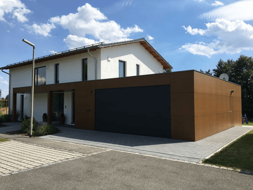Modernes Haus mit braunem Garagentor, umgeben von einer gepflegten Landschaft und klaren Himmel.